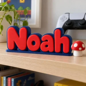 Prénom 3D Mario personnalisé à poser : lettres rouges et bleues sur une étagère d'enfant avec une manette en arrière-plan